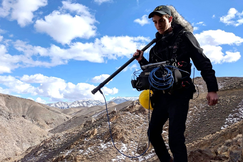 A boom operator hiking a snow-dusted desert ridge with a full bag rig